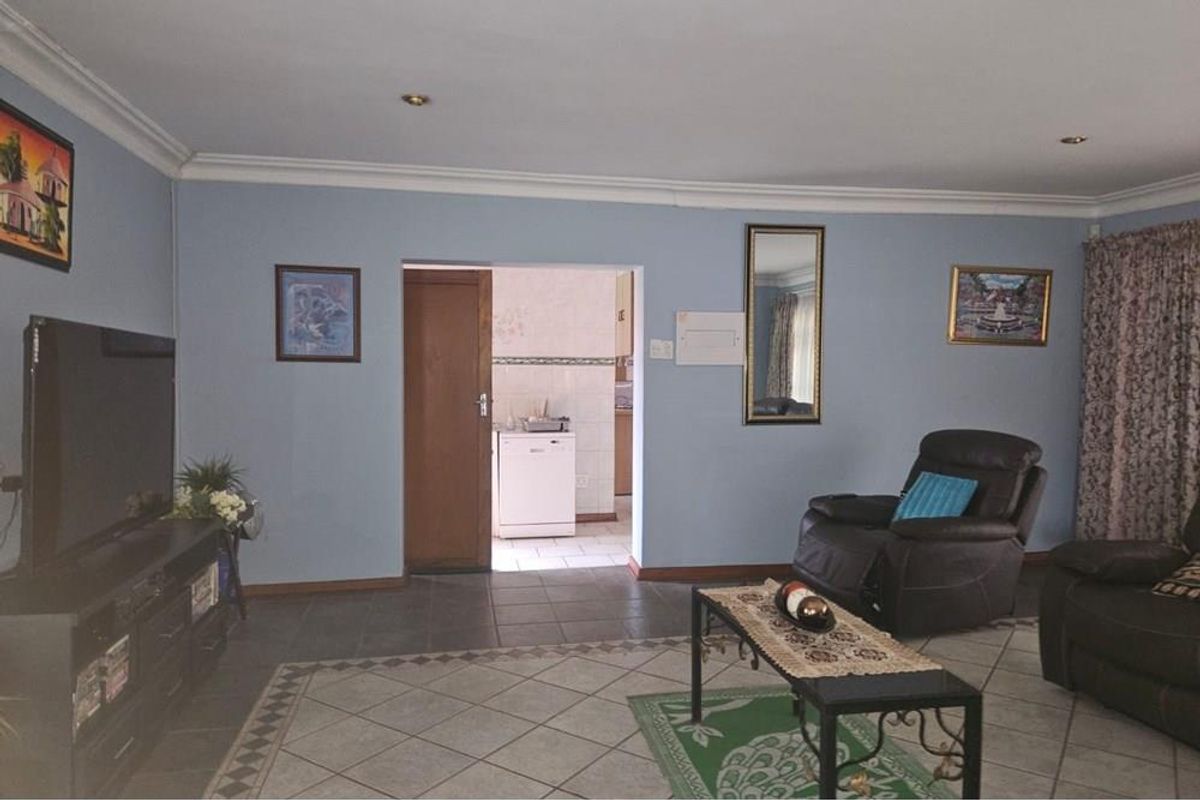 A living room featuring tiled flooring, crown molding, and recessed lighting, with a doorway leading to an adjacent kitchen area.
