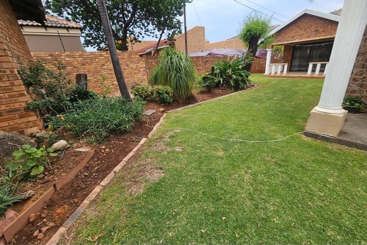 A private rear garden featuring a lawn area, established garden beds, and a brick boundary wall, adjacent to a covered patio space.