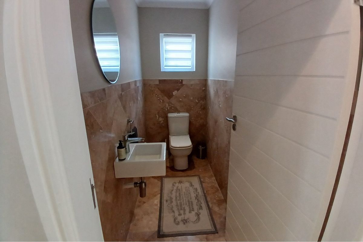 A compact guest bathroom featuring marble-style wall and floor tiling, a wall-mounted basin, and a modern toilet.