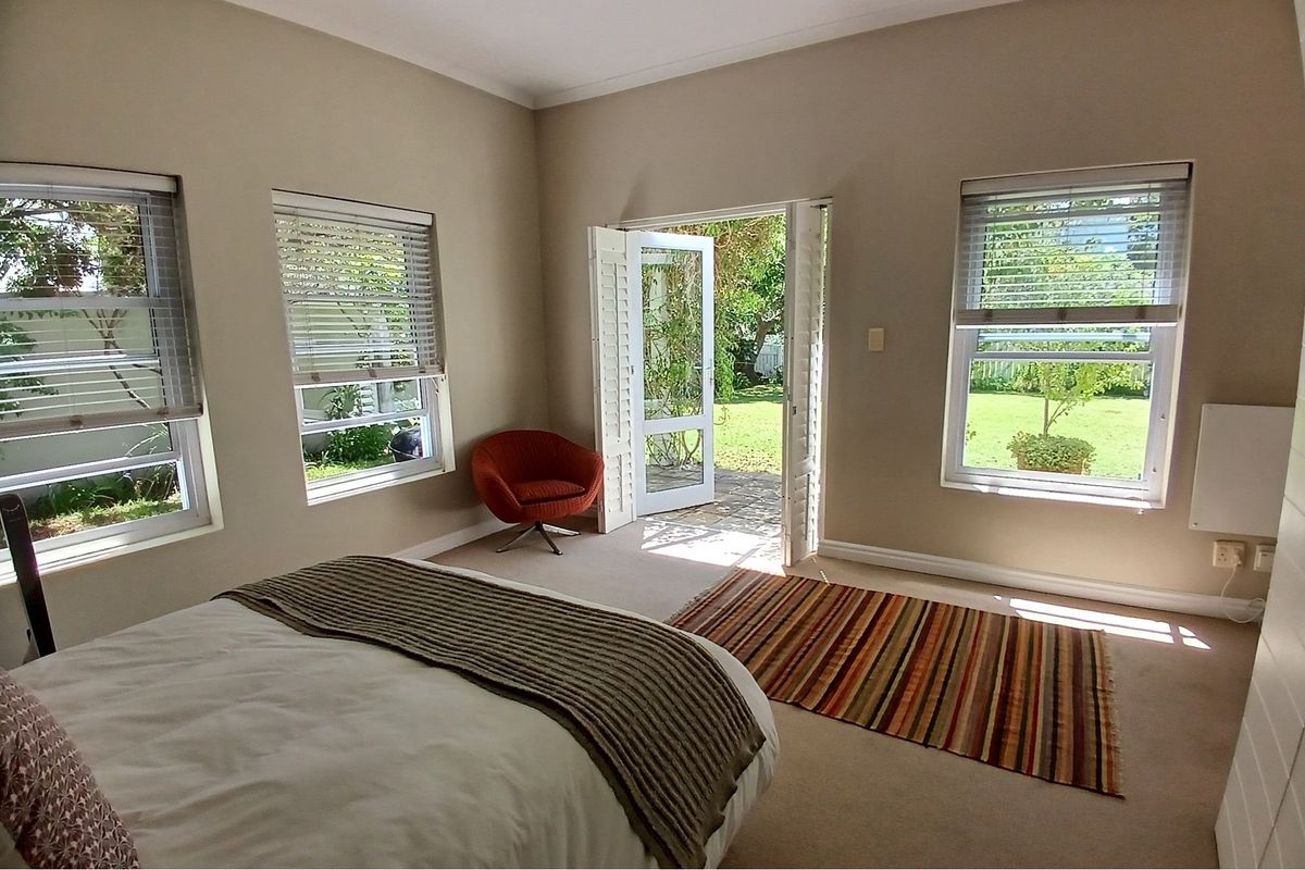 A bright bedroom featuring neutral walls, carpeted flooring, and direct access to the garden through a set of glass-paned double doors.