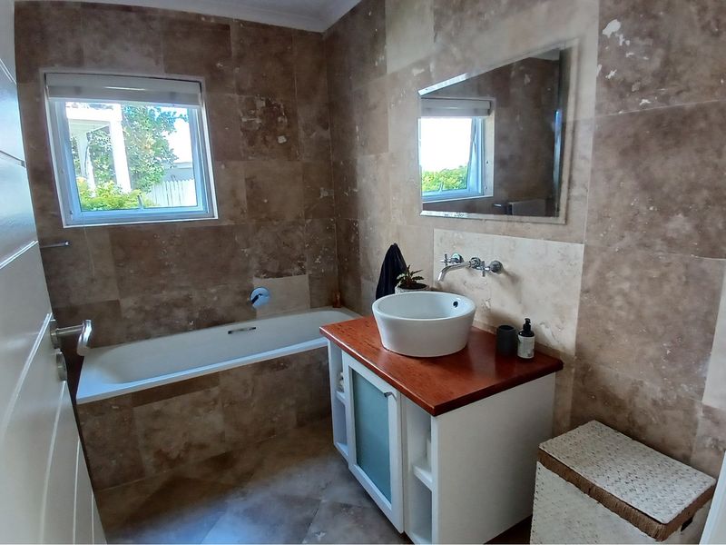 A bathroom featuring natural stone wall and floor tiles, a built-in bathtub, and a vanity unit with a vessel sink.