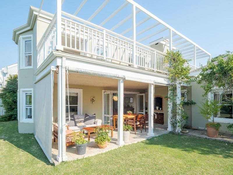 A spacious covered patio area featuring a built-in brick fireplace, overlooking a private garden with an upper-level balcony above.