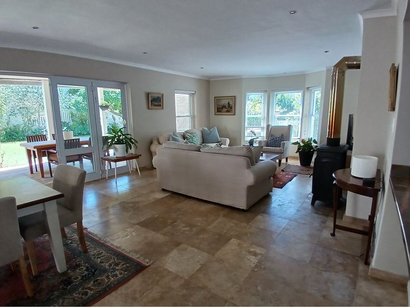 Spacious open-plan living and dining area featuring natural stone flooring, a built-in fireplace, and large glass doors opening to the patio.