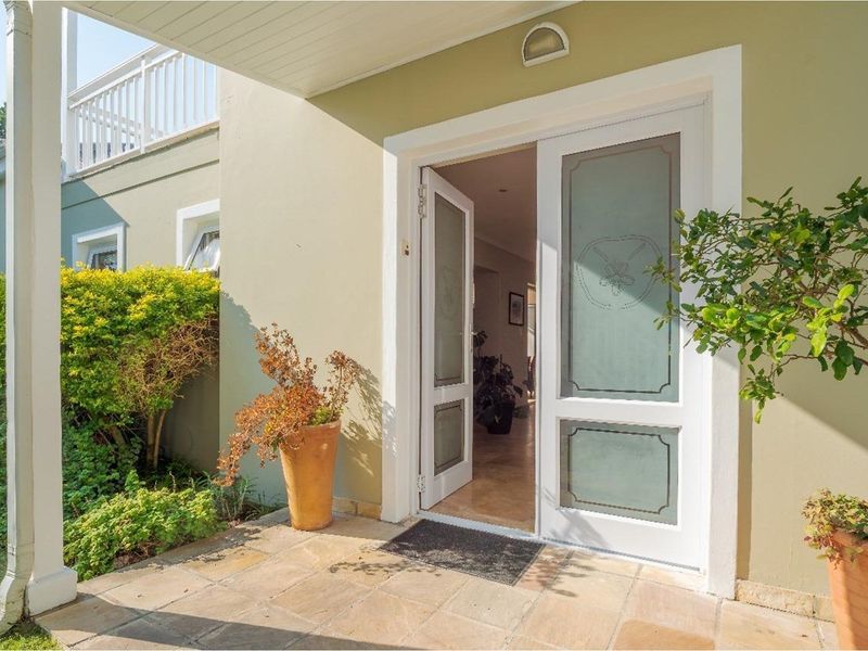 A welcoming covered patio entrance featuring stone paving, leading into the home through elegant glass-paneled double doors.