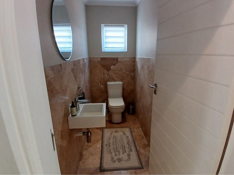 A compact guest bathroom featuring marble-style wall and floor tiling, a wall-mounted basin, and a modern toilet.