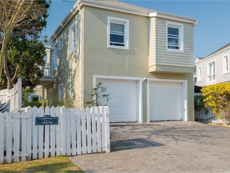 A two-story residential property featuring a double garage, paved driveway, and a white picket fence entrance.