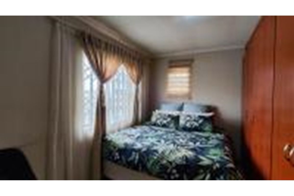 A compact bedroom featuring built-in wooden cabinetry and a window with fitted blinds.