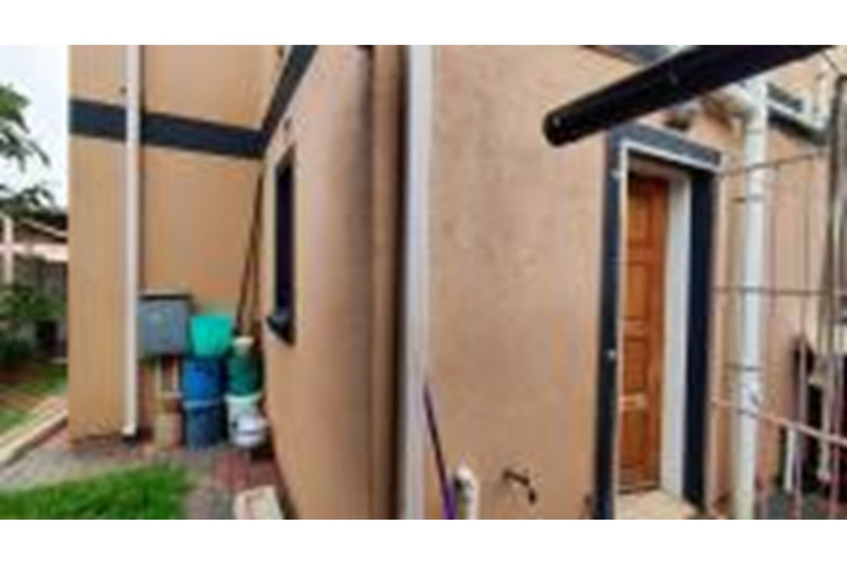 A side exterior view of the townhouse featuring a wooden door, downpipes, and paved ground area.