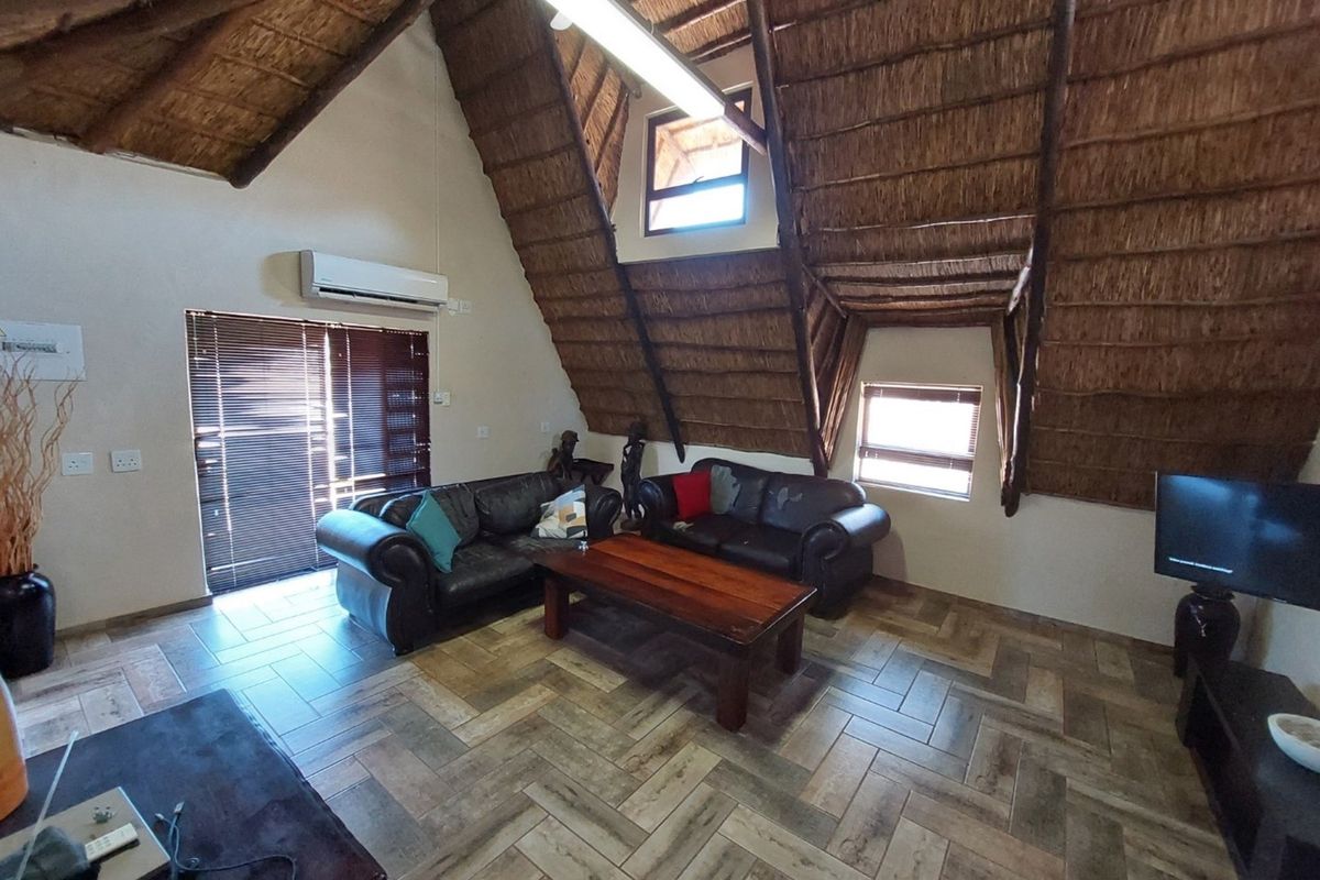 Spacious living area featuring a high vaulted thatched ceiling, exposed timber beams, tiled flooring, and a wall-mounted air conditioning unit.