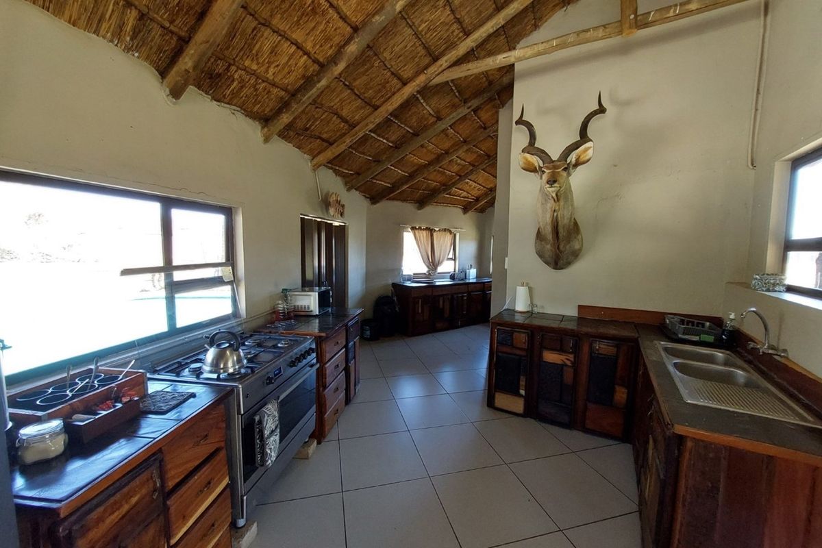Rustic farm-style kitchen featuring a high thatched ceiling, wooden cabinetry, a large gas stove, and double stainless steel sink.