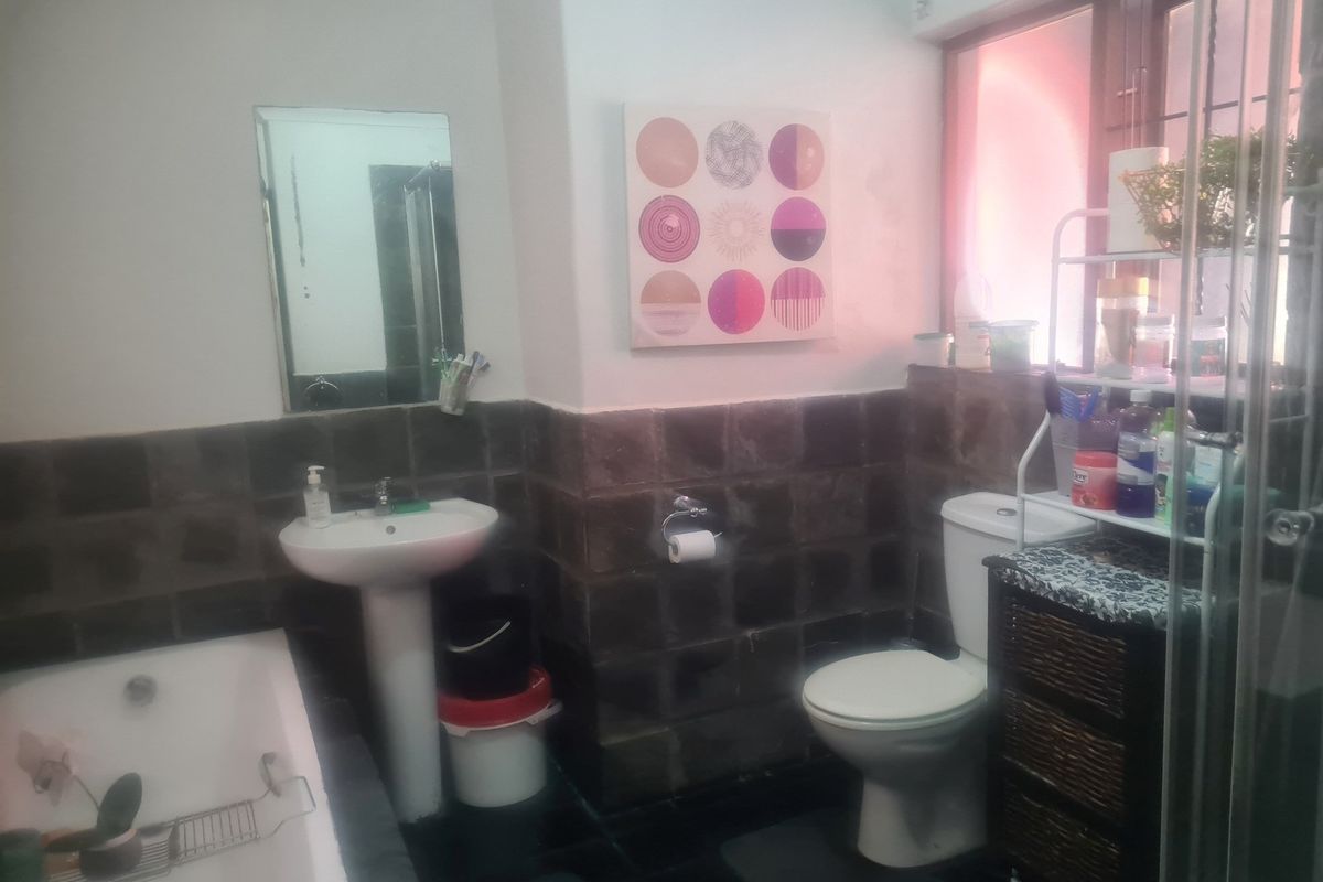 A dated bathroom featuring a pedestal basin, standard toilet, and bathtub with dark stone-style wall tiling and a wall-mounted mirror.