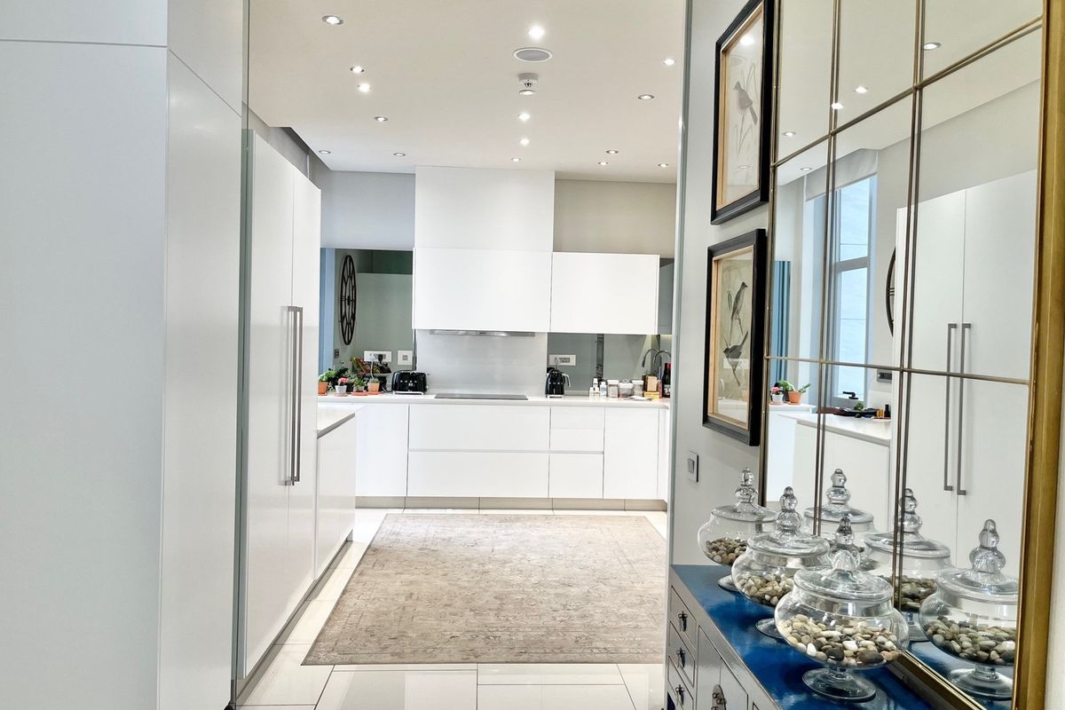 Modern kitchen featuring sleek white cabinetry, integrated appliances, recessed ceiling lighting, and polished floor tiles in a clean, minimalist design.