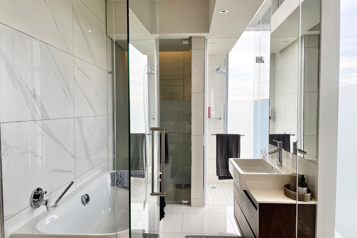 Modern penthouse bathroom featuring marble-look wall tiles, a sleek freestanding bathtub, a glass-enclosed shower, and a contemporary vanity with integrated basin.