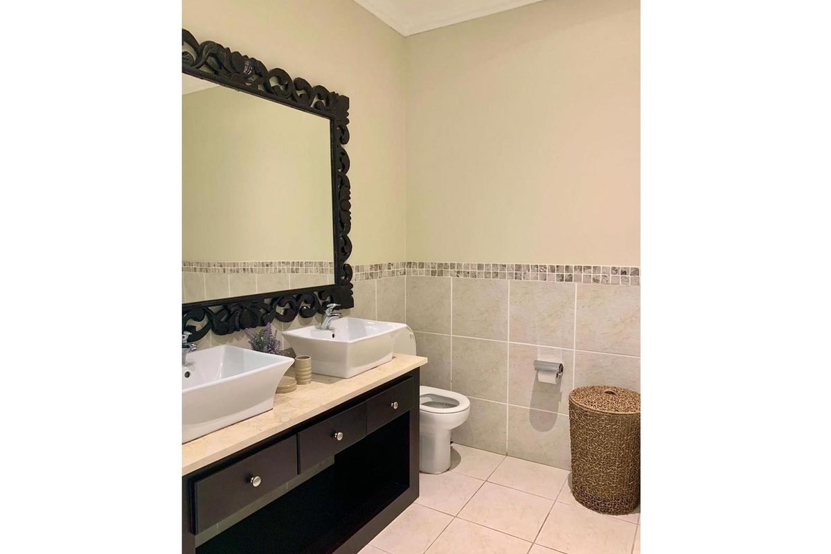 A bathroom featuring a double vanity with vessel sinks, a toilet, and tiled walls with a decorative mosaic border.