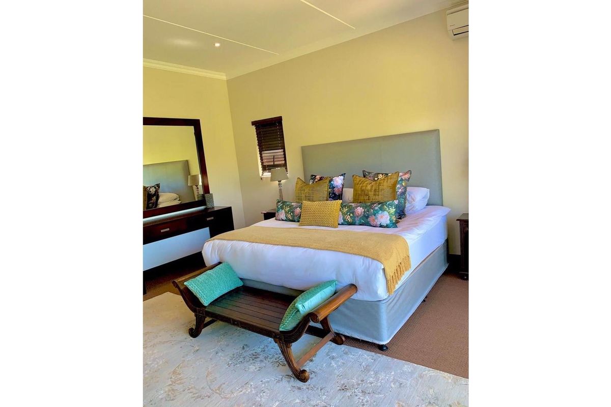 A well-maintained bedroom featuring neutral wall tones, a wall-mounted air conditioning unit, and a window with fitted blinds.