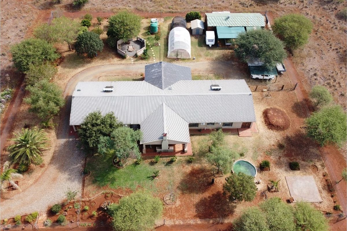 Aerial view of a rural property featuring a large house with a metal roof, swimming pool, outbuildings, and extensive grounds.