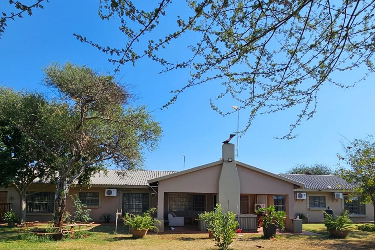 Rear view of the house featuring a covered patio, external chimney, and established garden surroundings.