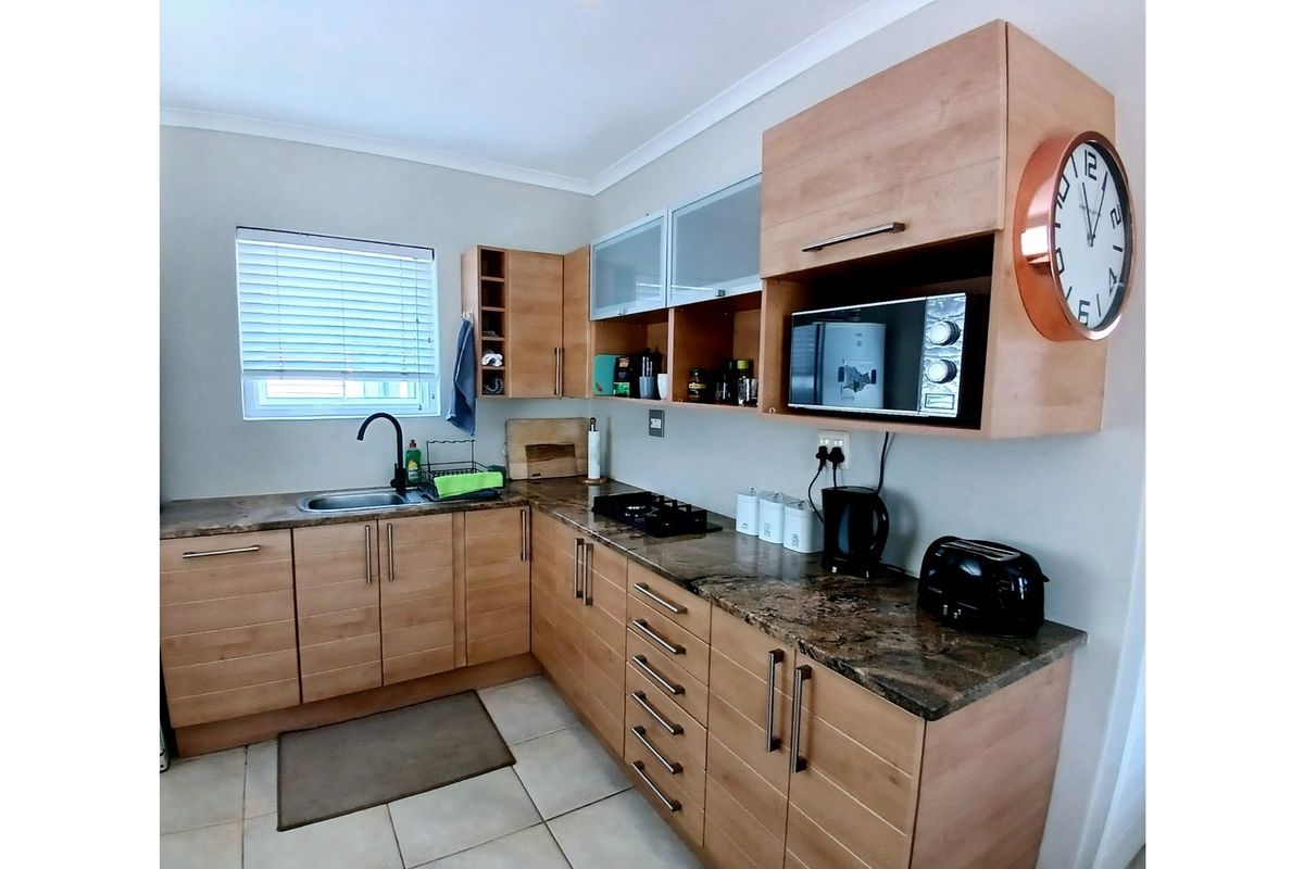 A functional kitchen featuring light wood cabinetry, granite countertops, a built-in hob, and a stainless steel sink with a modern black faucet.