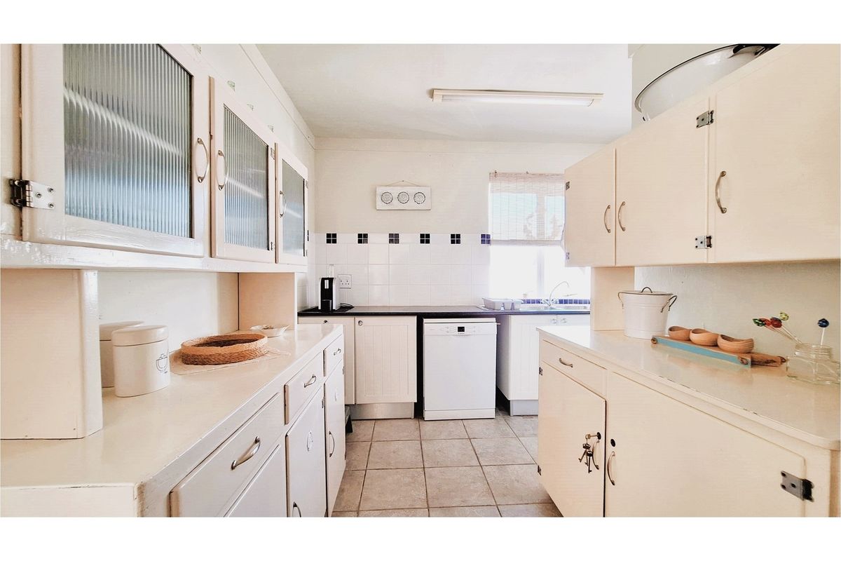 A functional kitchen featuring white cabinetry, tiled splashbacks, and tiled flooring, offering a classic layout with ample storage space.