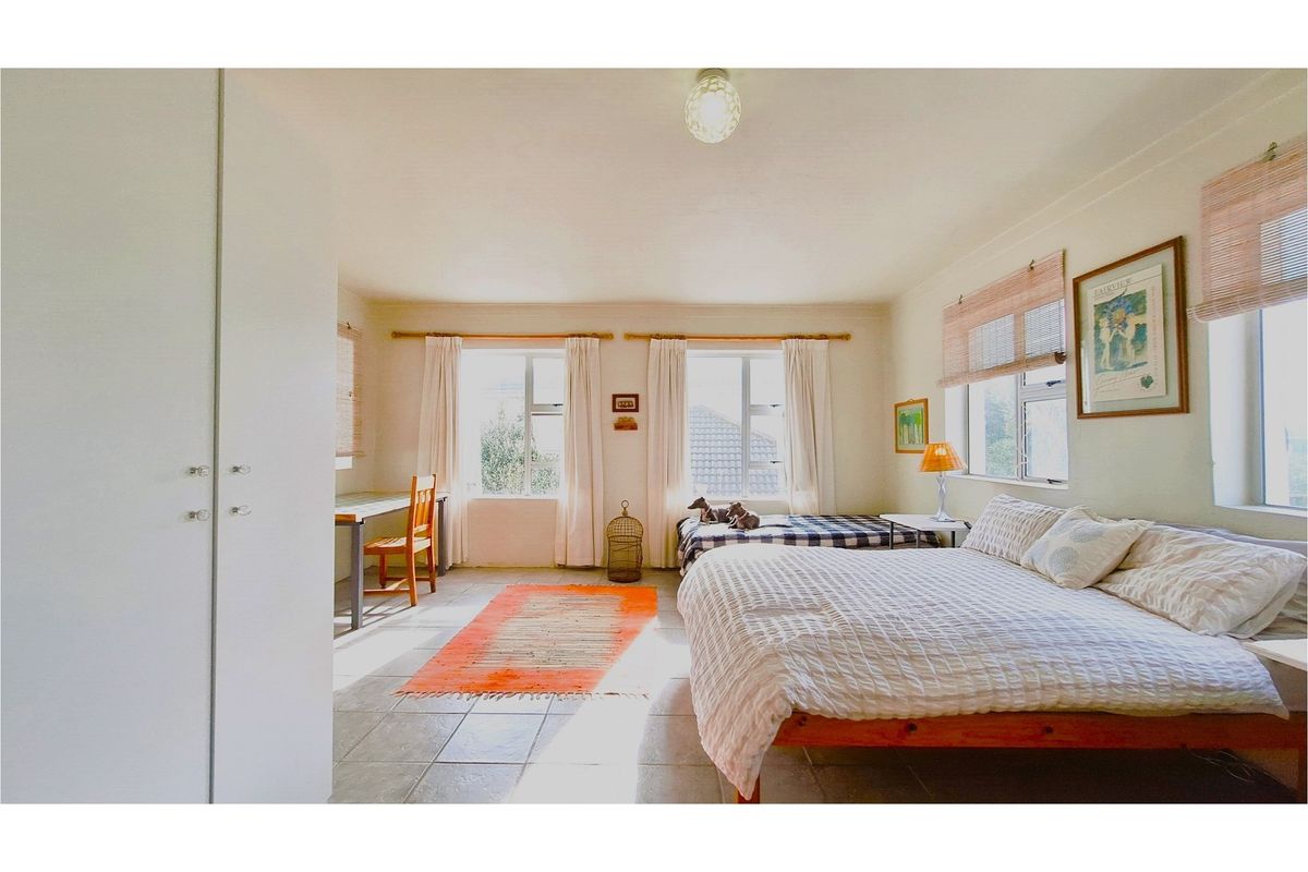A spacious bedroom featuring tiled flooring, built-in cupboards, and multiple windows providing ample natural light.