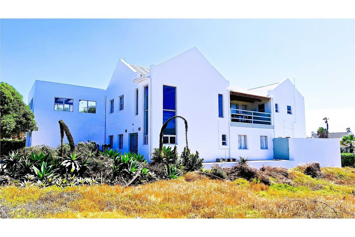 A view of the rear elevation of a multi-story house featuring a balcony, white exterior walls, and landscaped garden area.