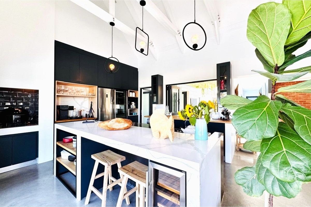 Modern open-plan kitchen featuring sleek black cabinetry, a large stone-topped island with integrated wine cooler, and exposed vaulted ceiling beams.