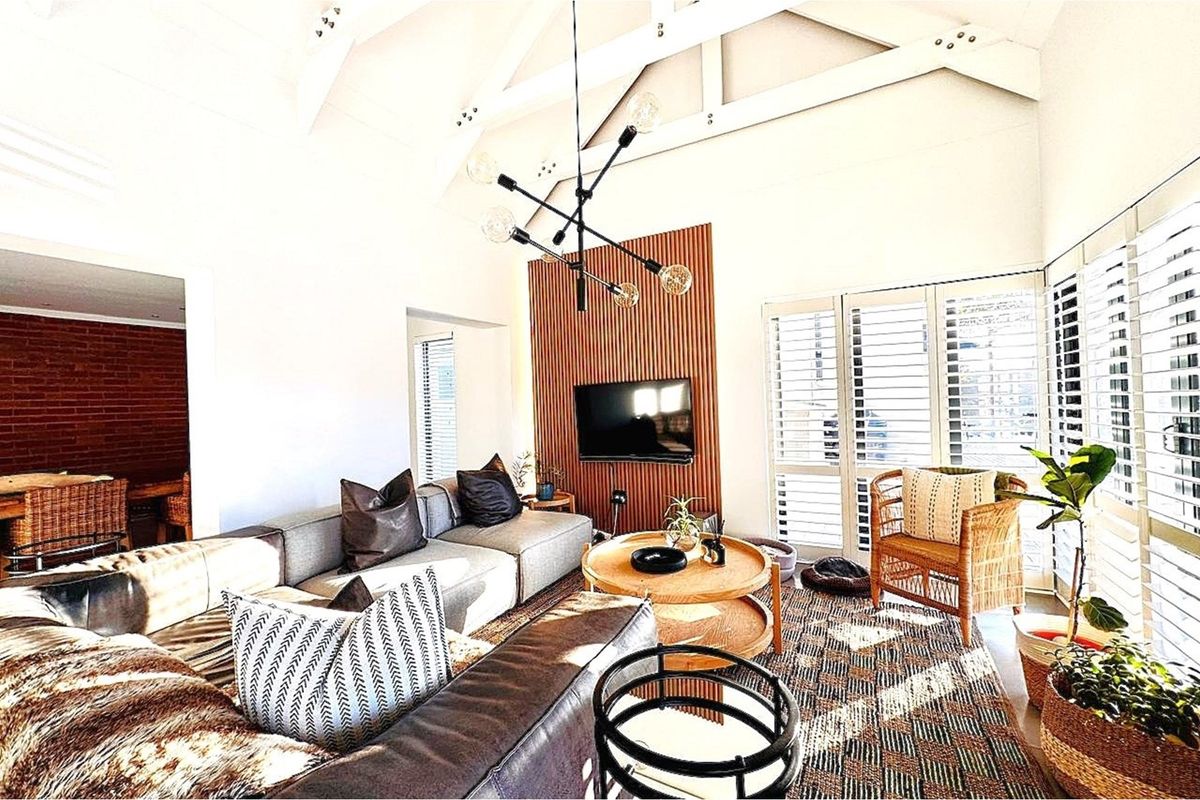 Spacious living room featuring high vaulted ceilings with exposed beams, a modern slatted wood feature wall, and large windows with plantation shutters.