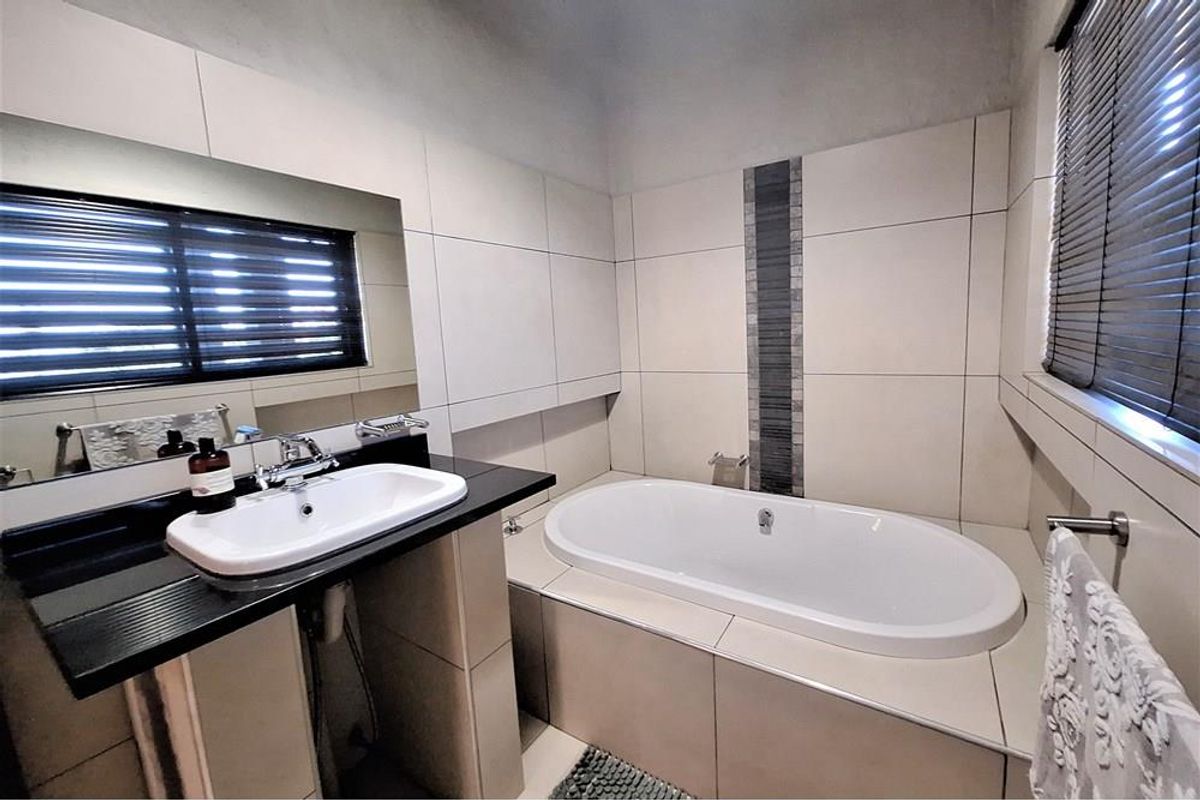 Modern bathroom featuring a built-in bathtub, a vanity with a countertop basin, and neutral wall tiling with a decorative mosaic accent strip.