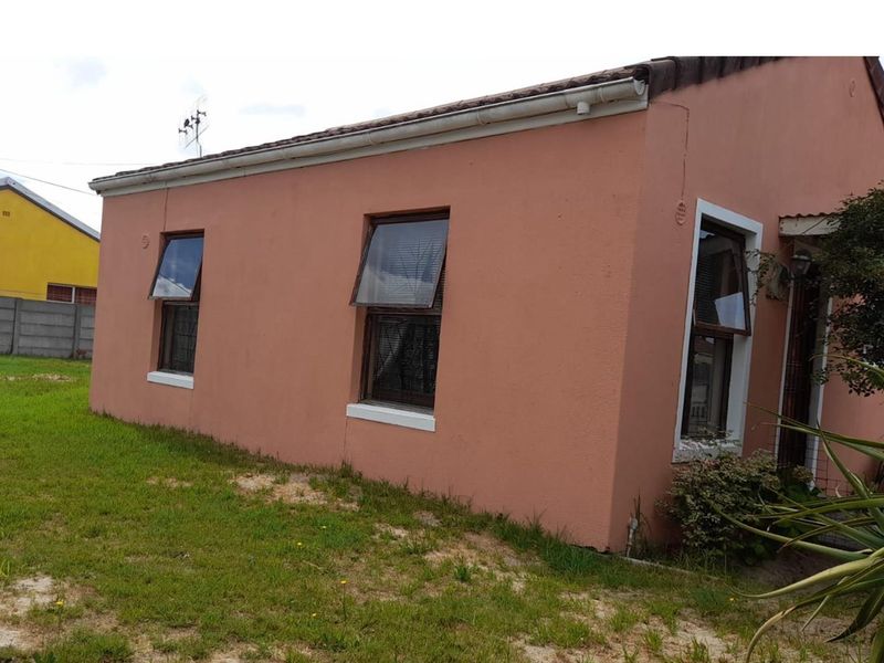 Side view of a residential house featuring a pink stucco facade, top-hung windows, and a tiled roof, set on a grassed plot.
