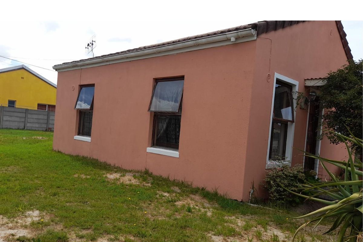 Side view of a residential house featuring a pink stucco facade, top-hung windows, and a tiled roof, set on a grassed plot.