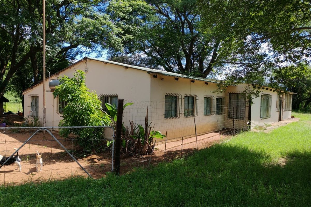 Exterior view of a single-story small holding dwelling featuring a metal roof, security bars on windows, and a fenced yard area.