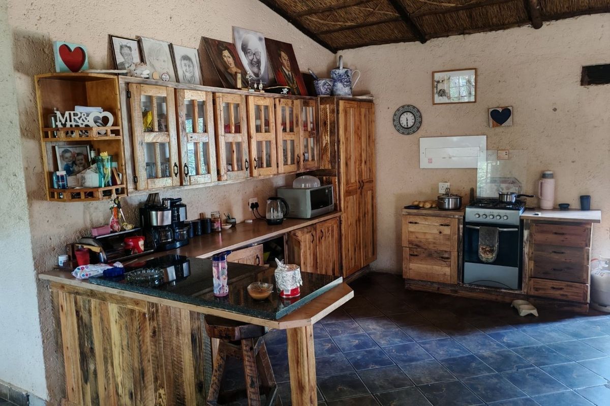 Rustic kitchen featuring custom wooden cabinetry, granite countertops, a gas stove, and a traditional thatched ceiling with tiled flooring.