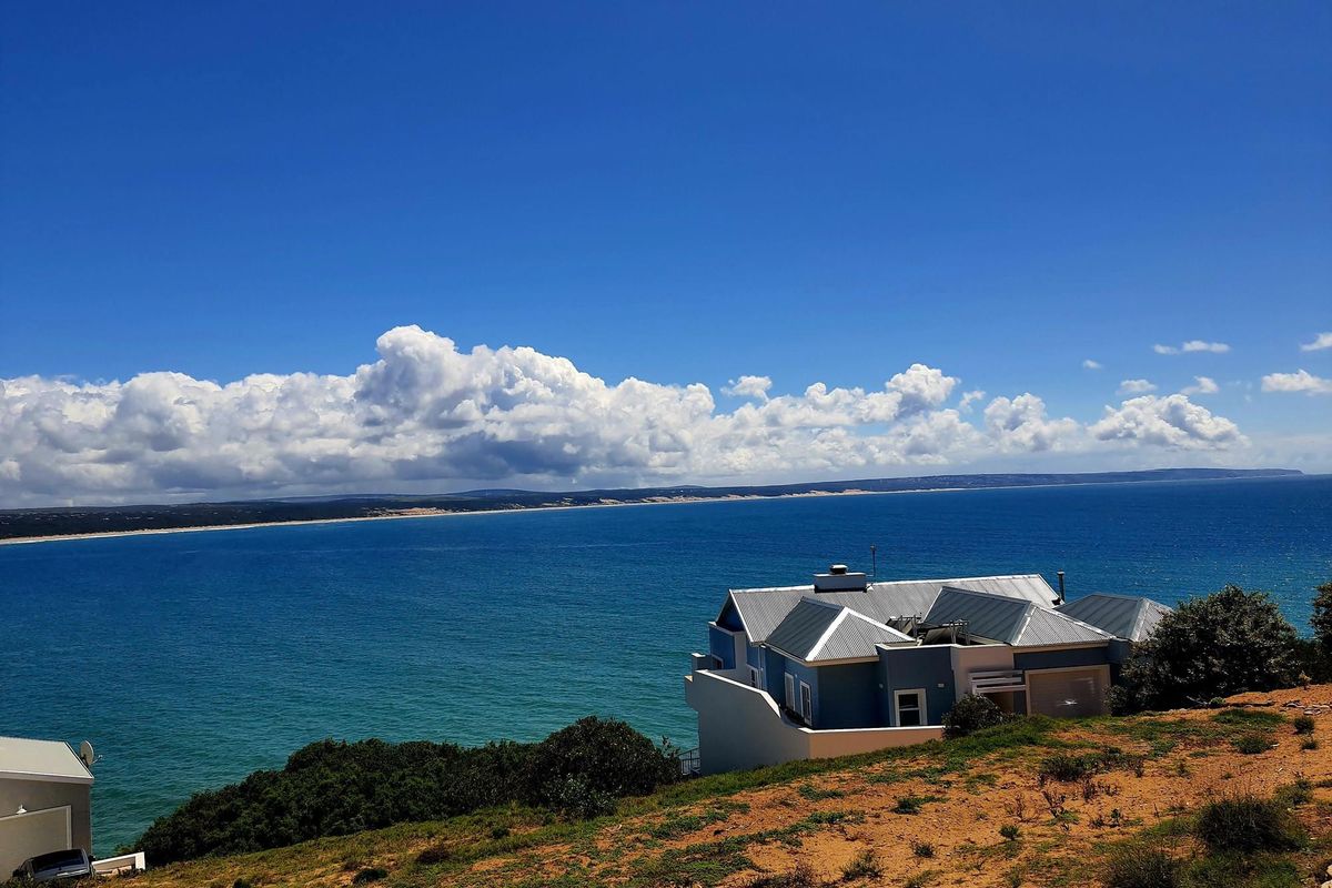 Elevated aerial view showcasing a coastal residential property with expansive ocean views and a clear horizon.
