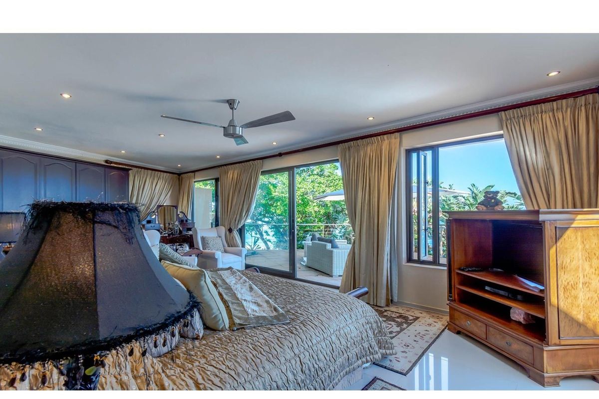 Spacious bedroom featuring tiled floors, recessed lighting, a ceiling fan, and large sliding glass doors opening onto a private balcony with garden views.