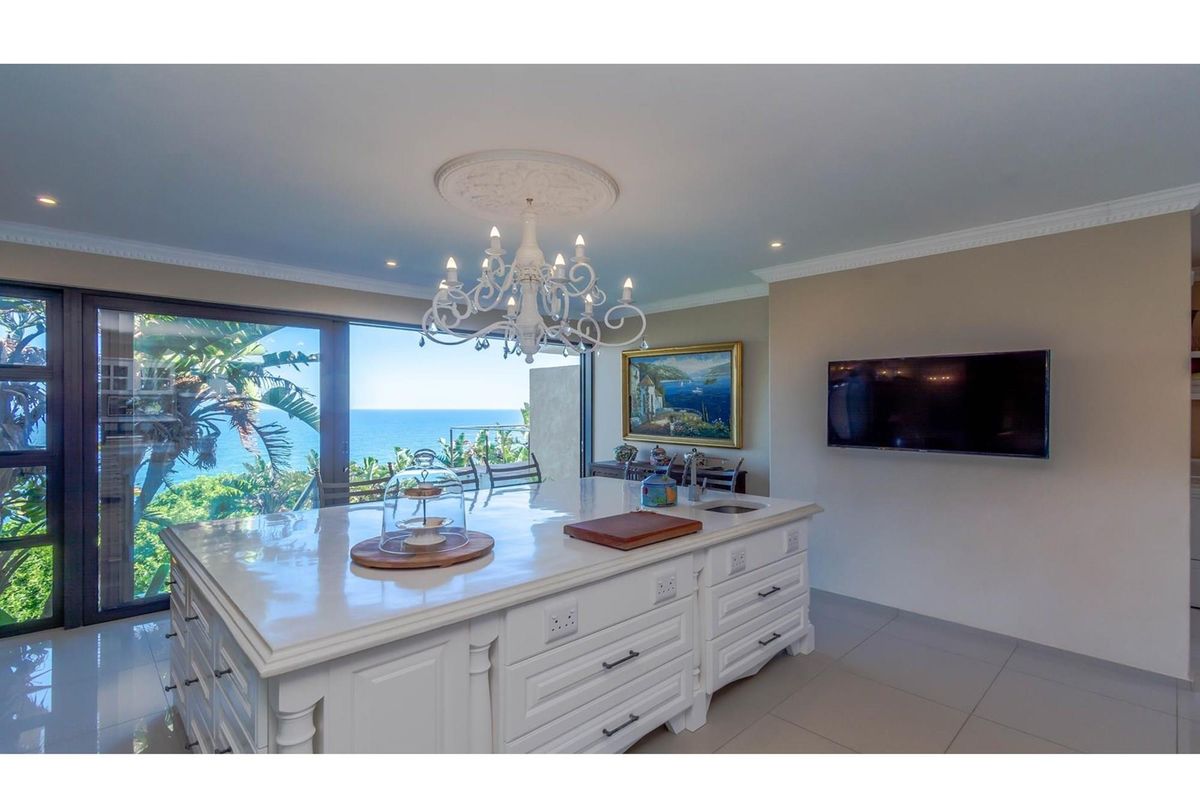 Modern kitchen featuring a large central island with stone countertops, integrated cabinetry, and expansive sliding glass doors offering panoramic ocean views.