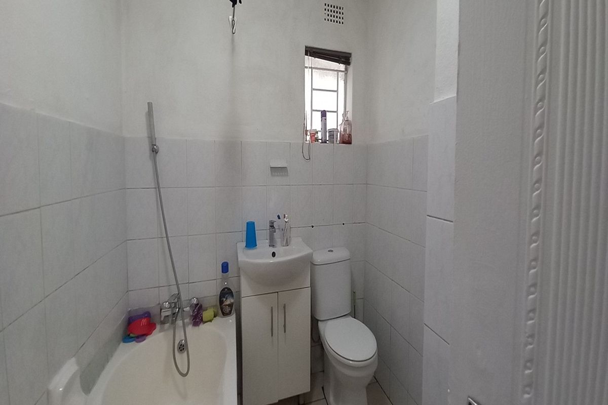 A compact bathroom featuring a white bathtub with handheld shower, a vanity basin, and a standard toilet with tiled walls.