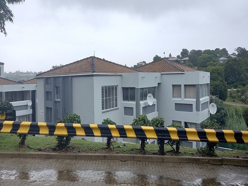Exterior view of a multi-story apartment complex featuring a tiled roof, grey facade, and paved driveway area.
