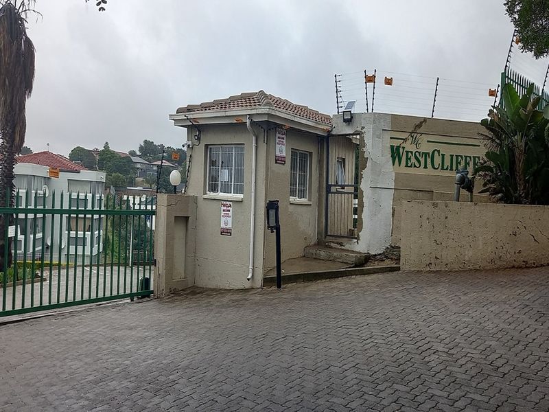 The entrance to The Westcliffe apartment complex, featuring a security guard house, paved driveway, and perimeter fencing with integrated security measures.