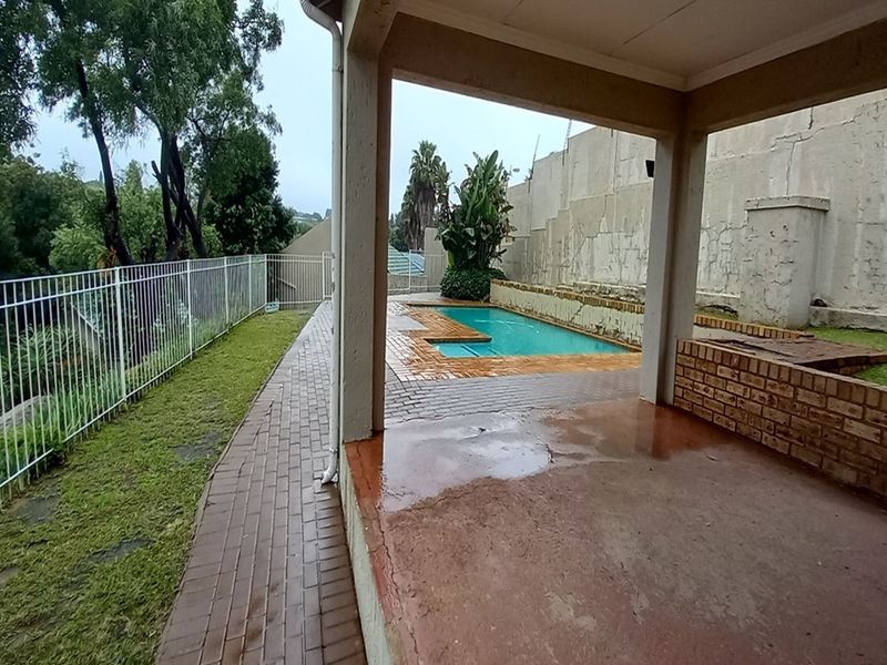 Covered patio area overlooking a swimming pool with brick paving and a perimeter fence, showing signs of weathering and wear.