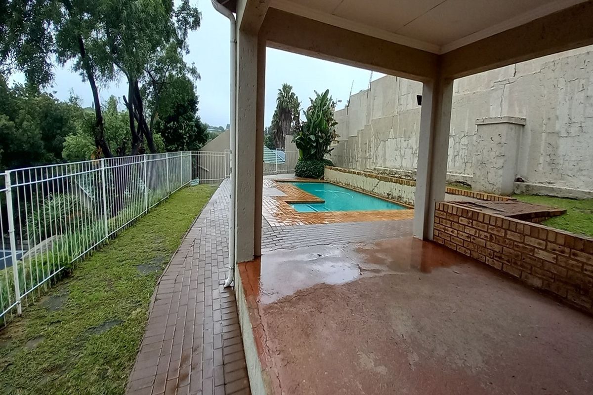 Covered patio area overlooking a swimming pool with brick paving and a perimeter fence, showing signs of weathering and wear.
