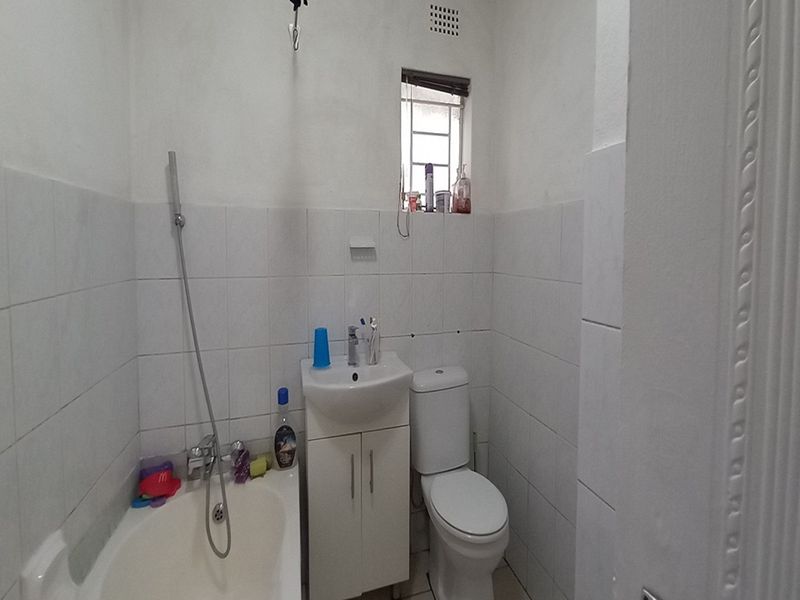 A compact bathroom featuring a white bathtub with handheld shower, a vanity basin, and a standard toilet with tiled walls.