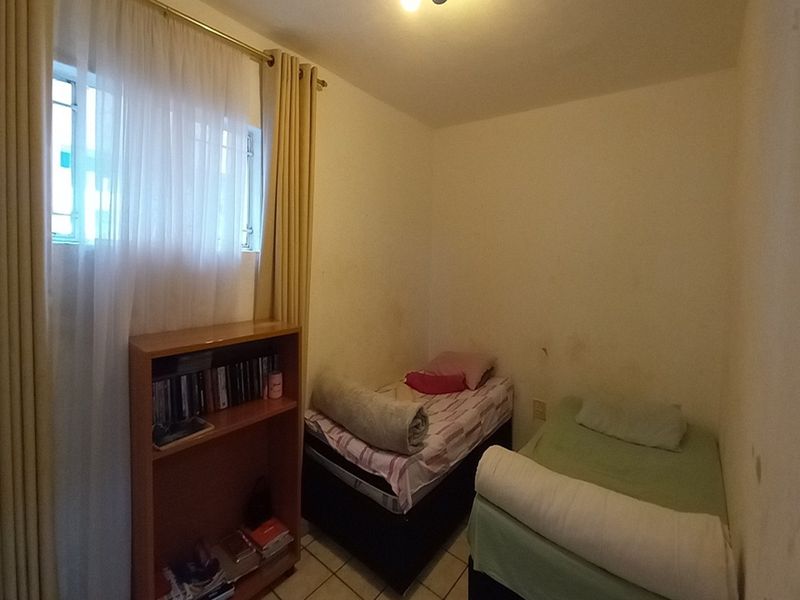 A compact bedroom featuring tiled flooring, a high-set window with security bars, and neutral wall finishes.