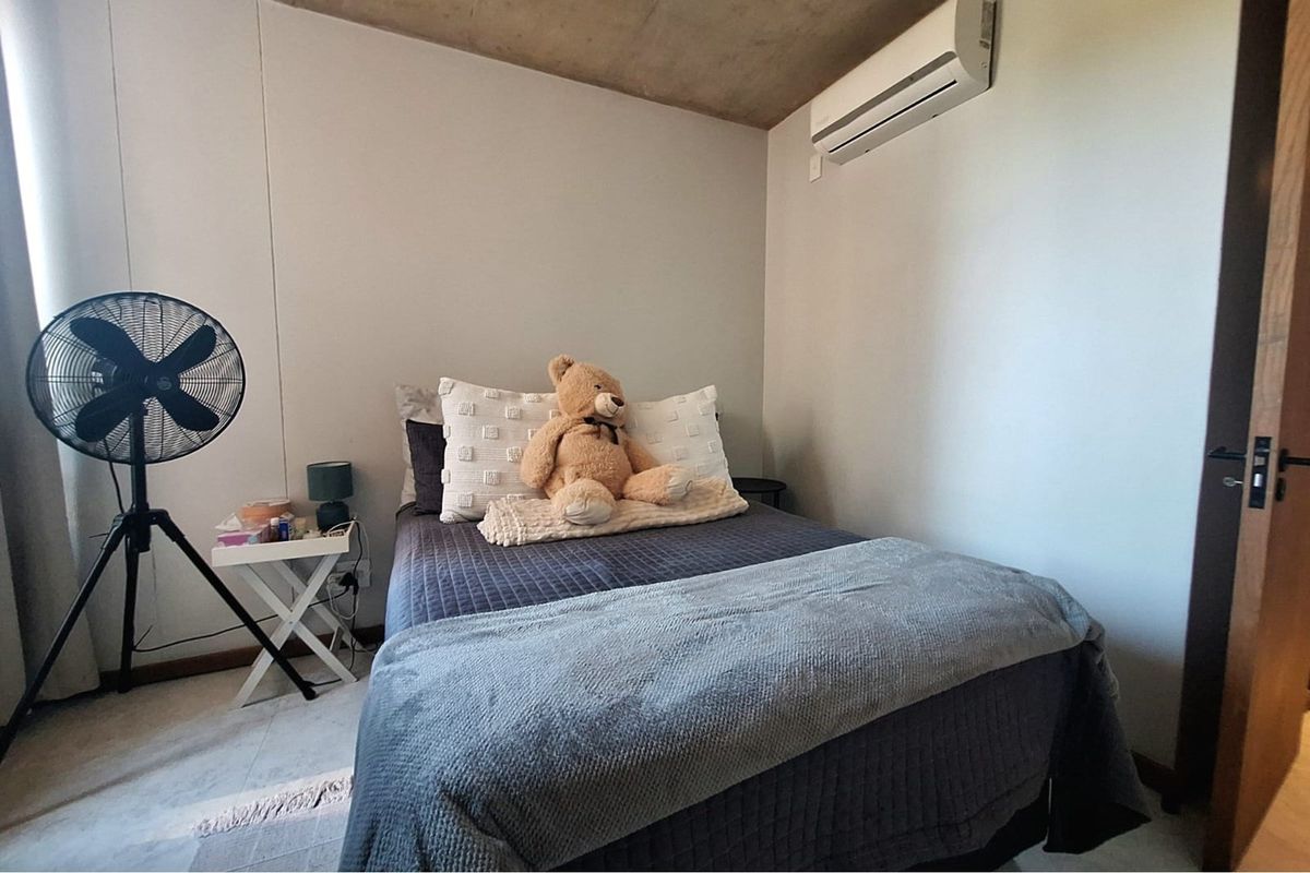 A cozy bedroom featuring a split-system air conditioning unit and a raw concrete ceiling finish.