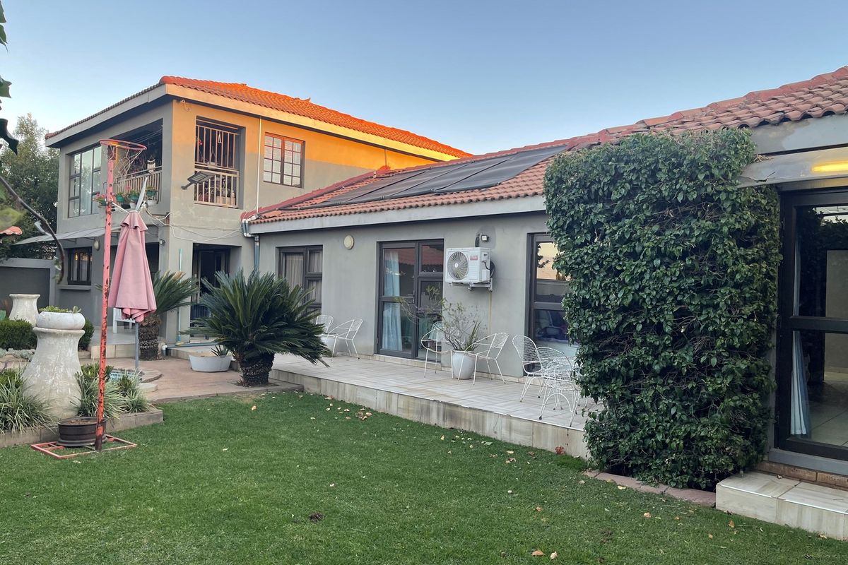 Rear view of the property featuring a tiled patio area, established garden, and solar water heating panels installed on the roof.
