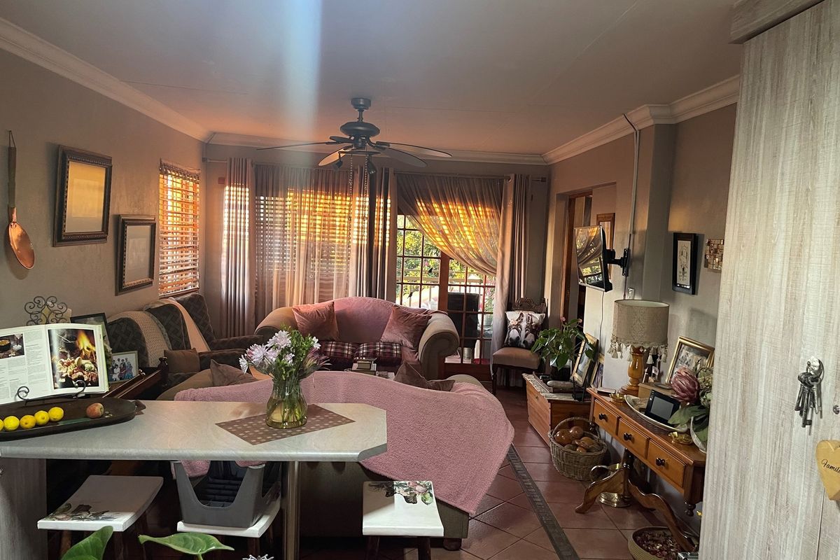 A cozy living room featuring tiled flooring, a ceiling fan, and large windows with blinds, providing a warm and inviting atmosphere.