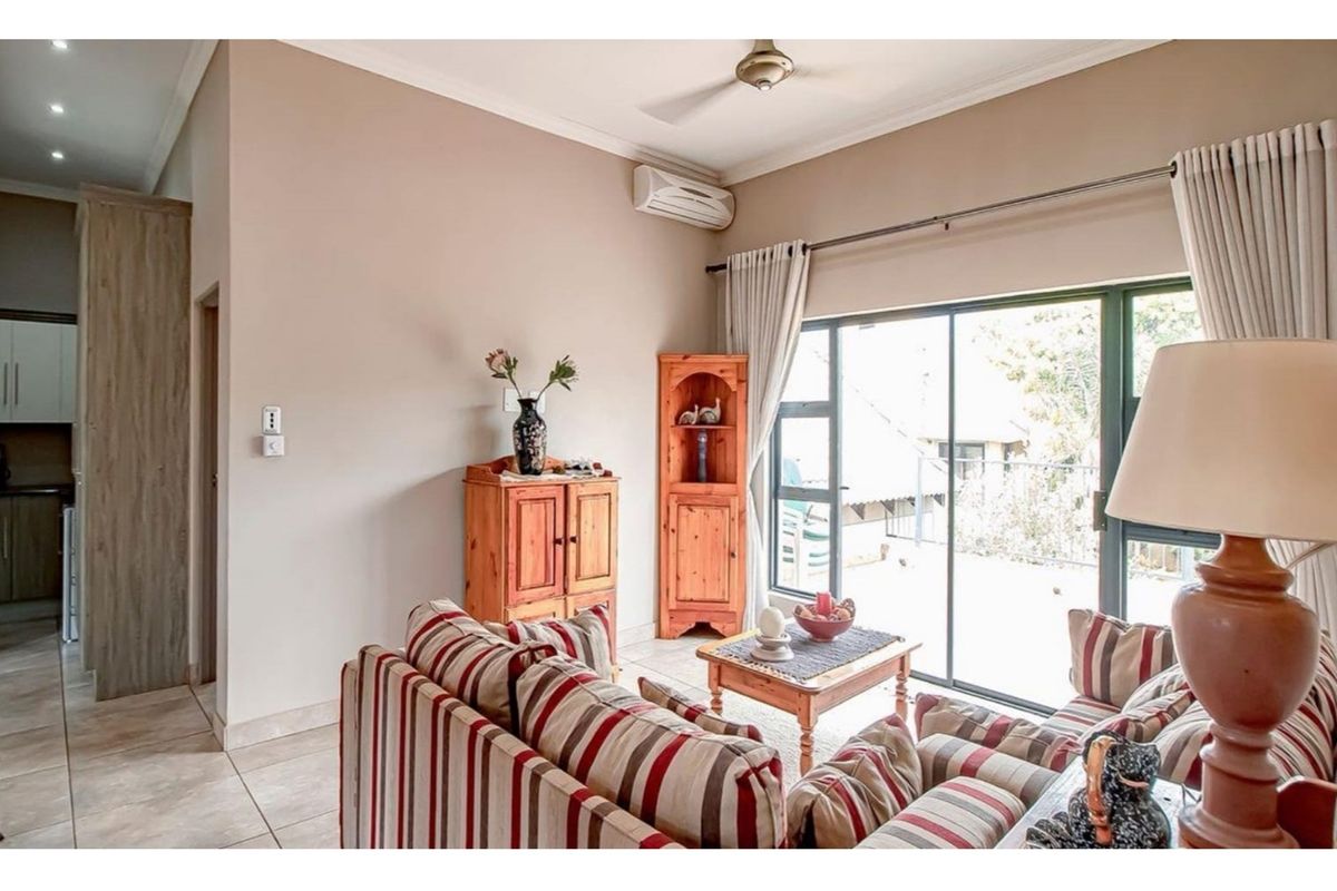 A comfortable living room featuring tiled flooring, a ceiling fan, a wall-mounted air conditioner, and large sliding glass doors leading to an outdoor area.