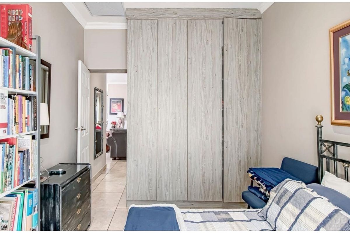 A bedroom featuring light wood-grain built-in cupboards, neutral wall tones, and tiled flooring, providing a functional and well-maintained living space.