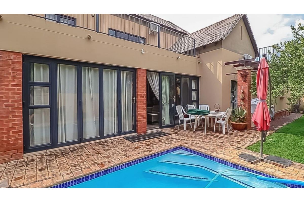 Rear exterior view featuring a swimming pool, paved patio area, and folding glass doors leading into the home with an upper-level balcony.