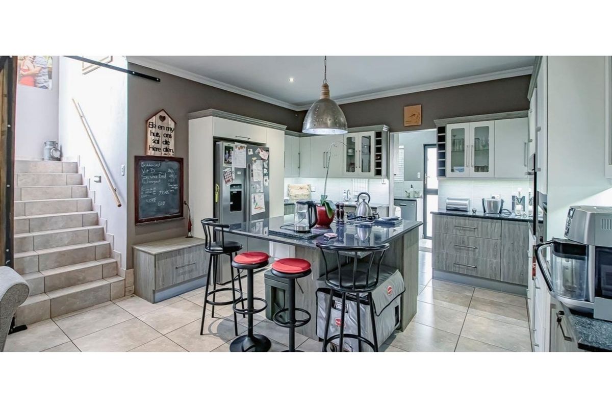 Modern kitchen featuring a central island with granite countertops, ample built-in cabinetry, tiled flooring, and integrated lighting, adjacent to an internal staircase.
