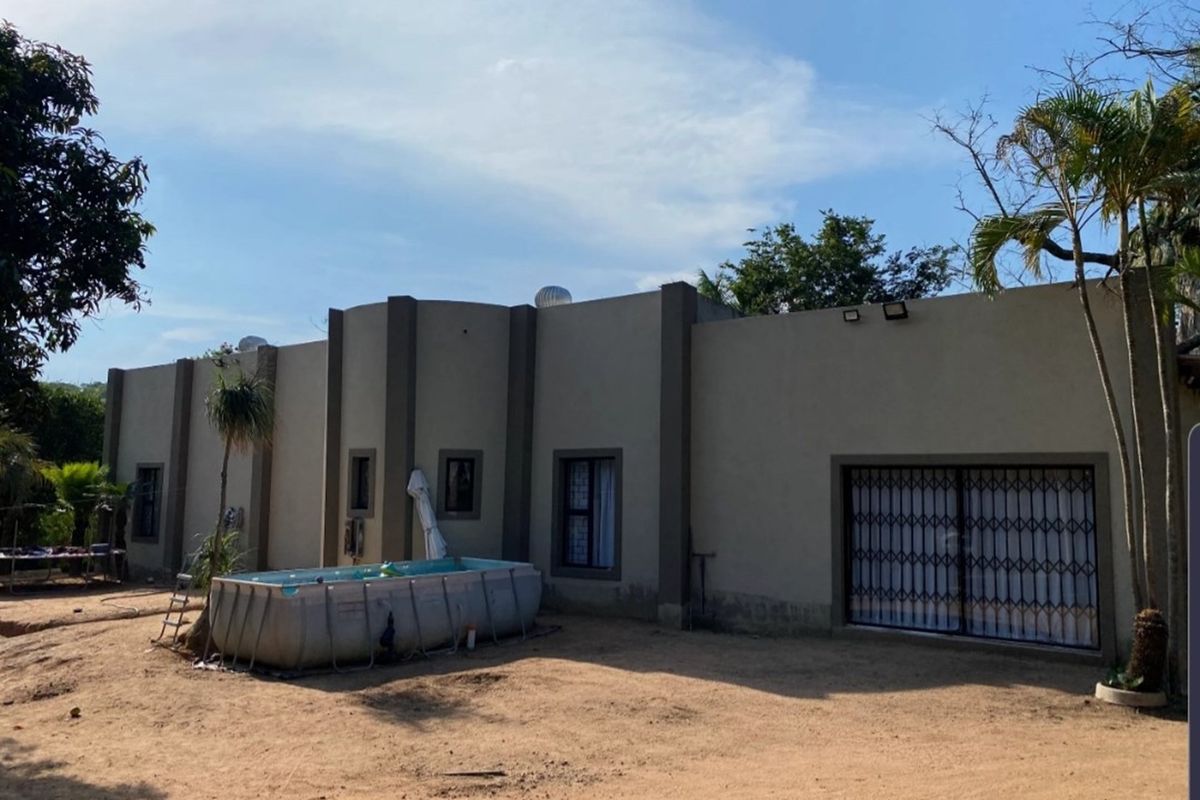 Rear exterior view of the farm property featuring a flat-roofed structure, security gates, and an above-ground pool in the yard.